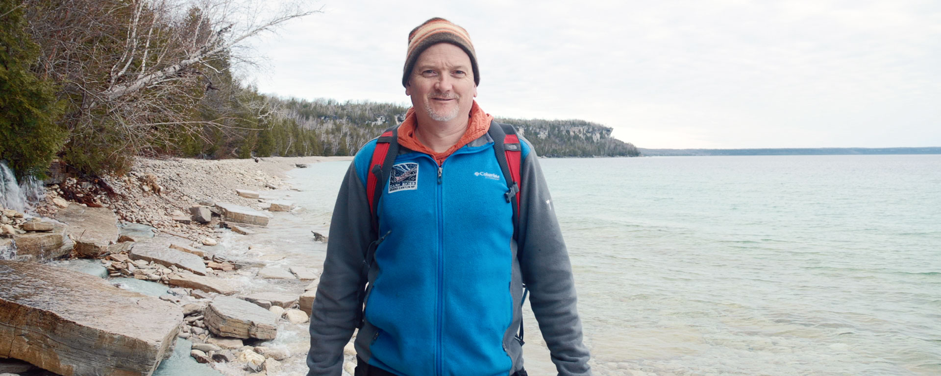 Man posing for the camera in blue jacket and hat ready for a hike