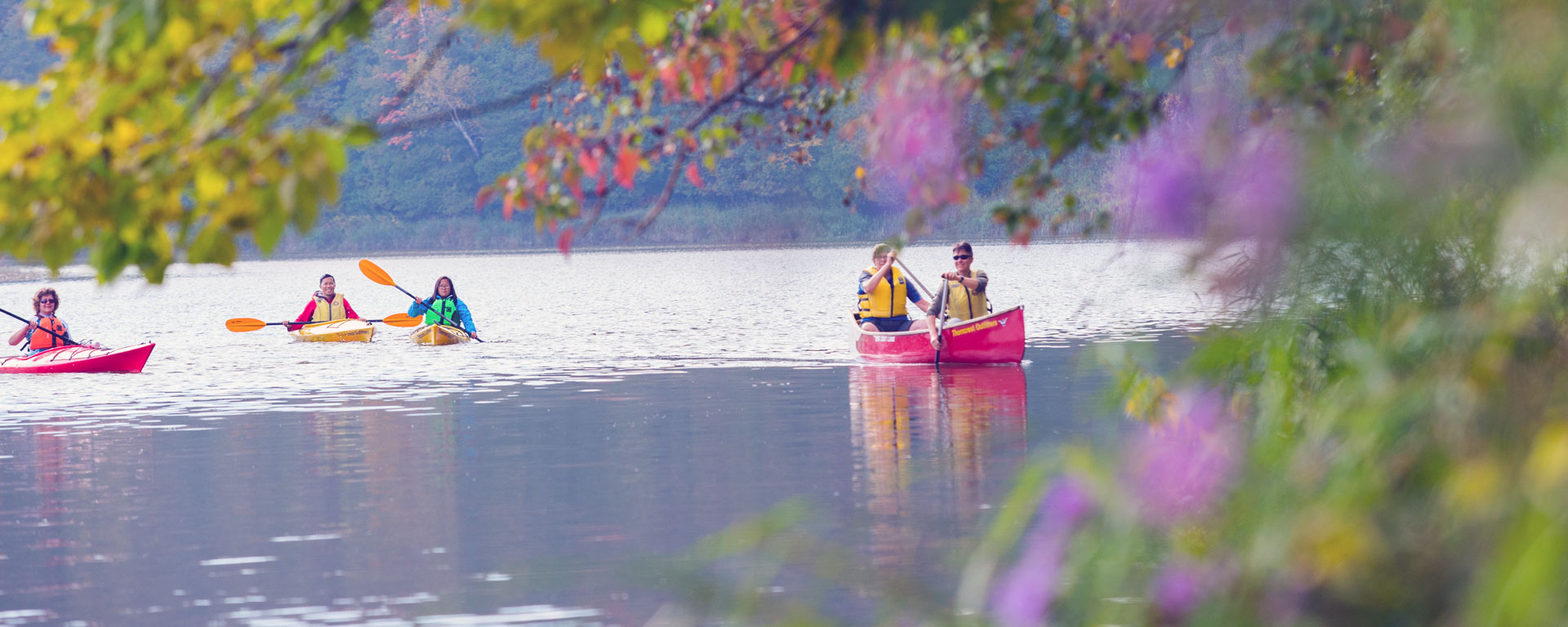 a group of people paddling on the river framed by out of focus foliage with purple flowers